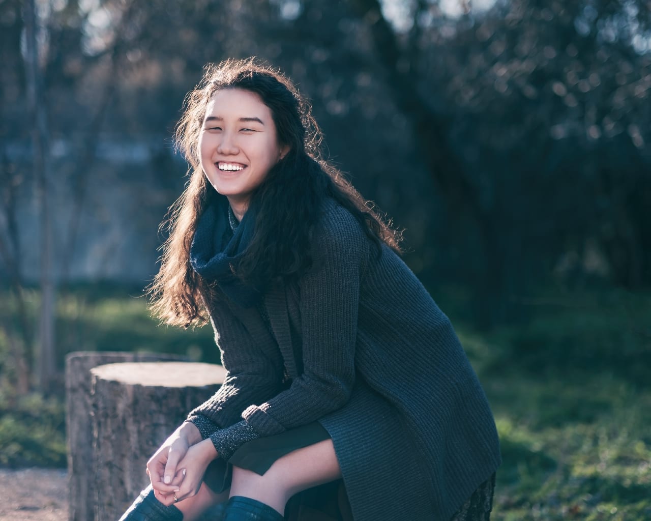 A beautiful Asian girl sits in a park on a stump and smiles. Enj happy patient waiting for gums to heal