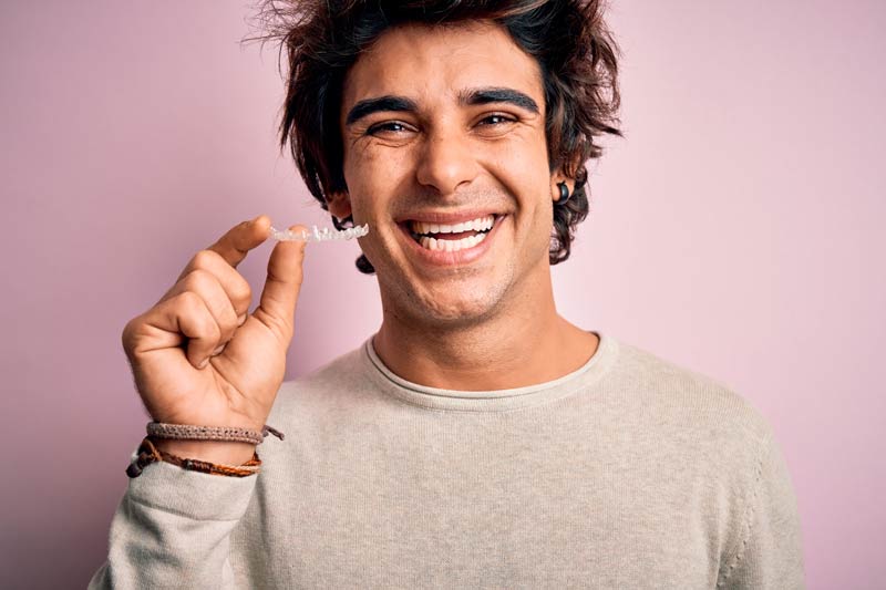 indian man smiling with a clear aligner in his hand
