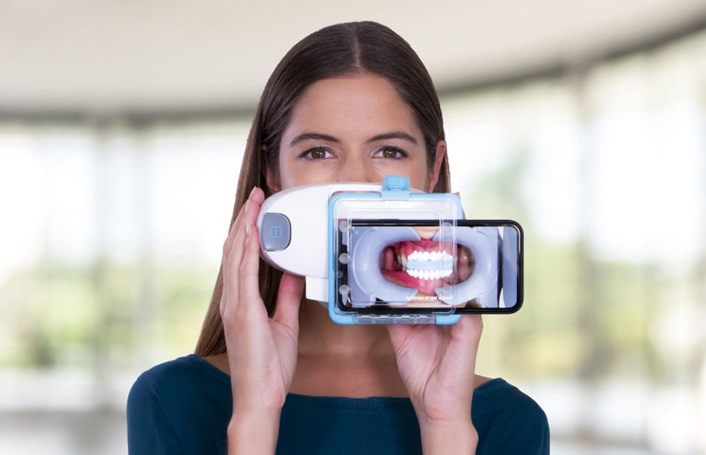 Woman using dental monitoring scanbox to scan and track her progress with Invisalign treatment